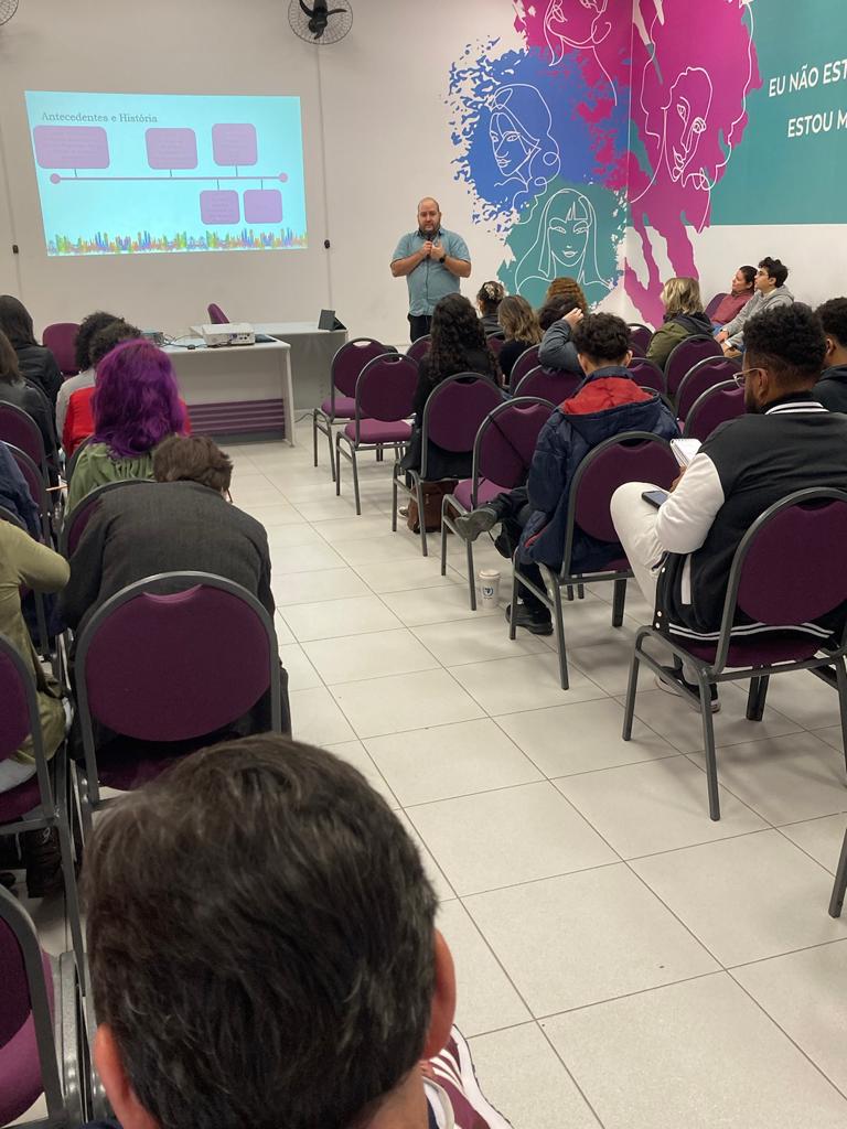 Alcyr Barbin Neto dando uma palestra no auditório da SMDH da PMSP, com projeção de slides.